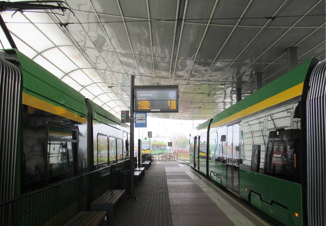 Zadaszony peron przystanku tramwajowego, po obu stronach peronu stoją tramwaje, nad peronem tablica świetlna z rozkładem jazdy - grafika artykułu