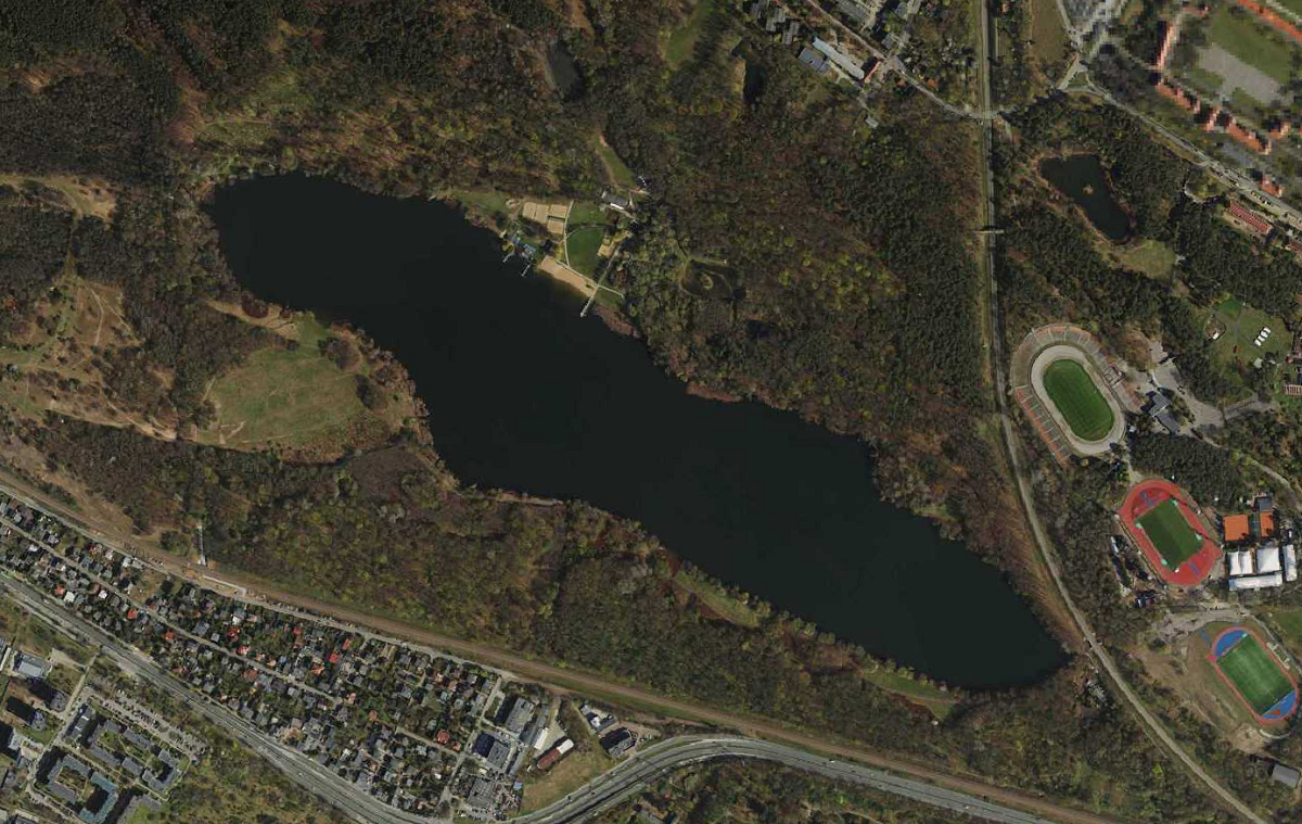 zdjęcie lotnicze z widokiem na ziezioro otoczone lasem, widoczne też obiekty sportowe stadiony - grafika artykułu