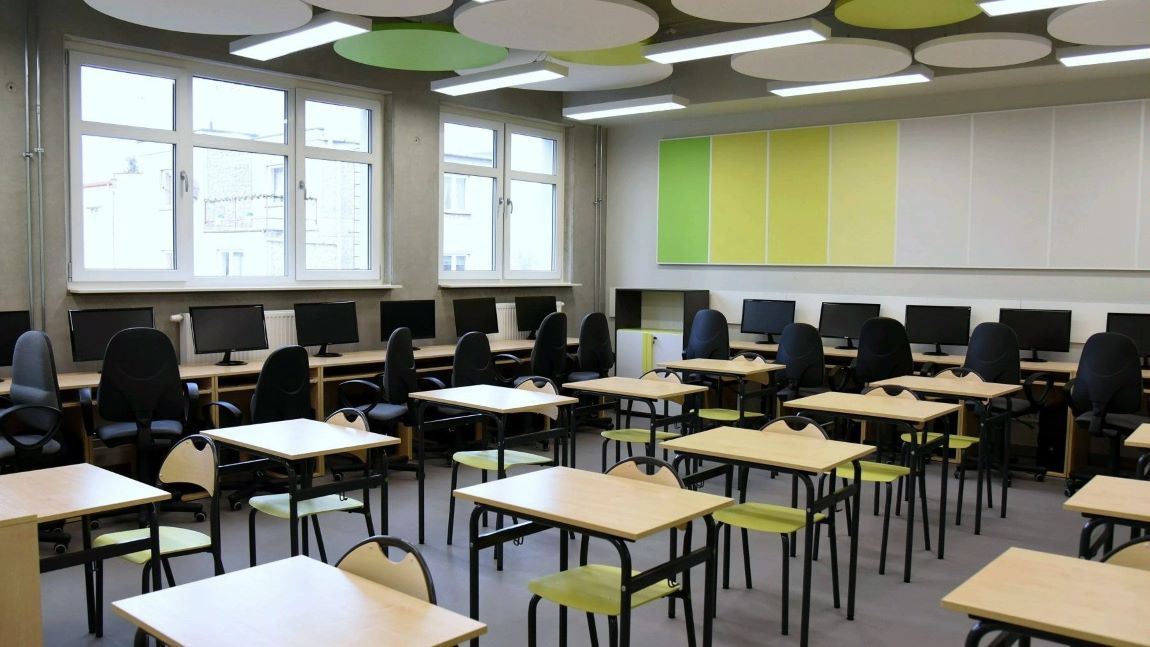 Klasa lekcyjna w szkole, pusta, stoliki i krzesła ustawione w rzędach, pod ścianami stanowiska z komputerami - grafika artykułu