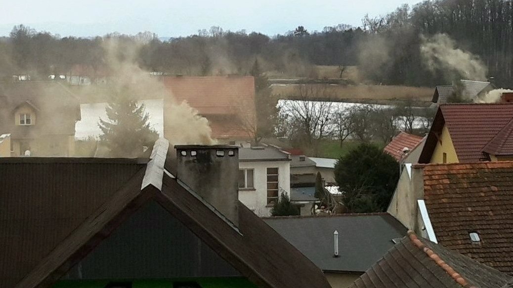 Na zdjeciu dachy kilku domów, z kominów wydobywa się gęsty szary dym - grafika artykułu