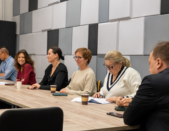 kilkoro osób kobiet i mężczyzn siedzi w sali przy stole konferencyjnym - grafika artykułu