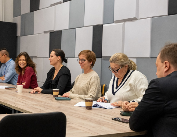 kilkoro osób siedzi w sali przy stole konferencyjnym - grafika artykułu