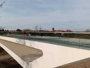 most pieszo rowerowy nad rzeką, ma szklane przejżyste balustrady na moście spacerują ludzie