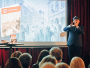 na zdjęciu mężczyna w mundurze grający na trąbce przed widownią, za nim na dużym ekranie wyświetlana jest prezentacja multimedialna - więcej w treści artykułu