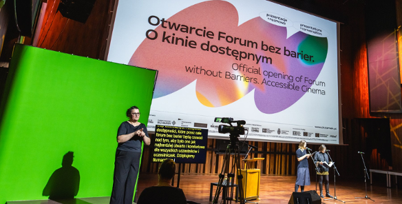 Na zdjęciu tłumacz polskiego języka migowego na zielonym tle. W tle plansza z informacją o otwarciu forum.