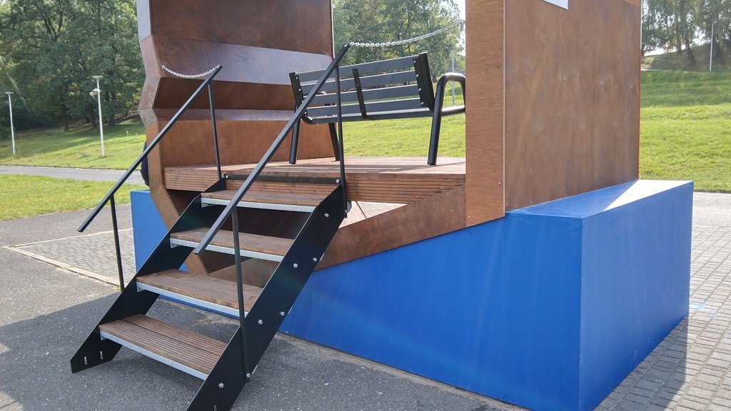 Siedzisko ławki znajduje się na podeście, do którego prowadzą schody