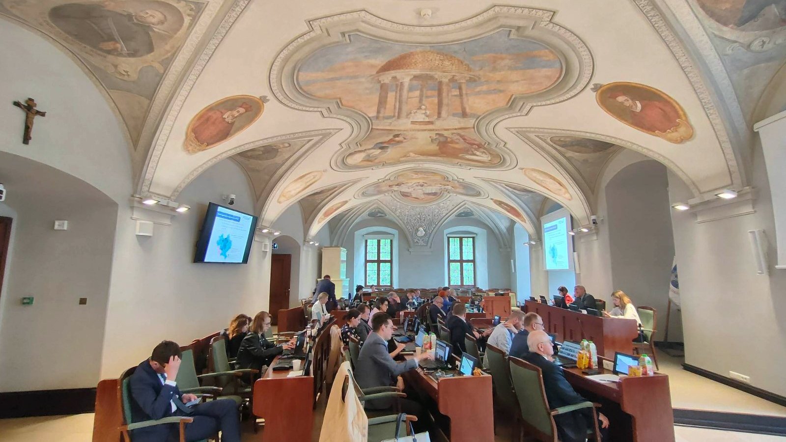 Radni poznańscy w czasie sesji, w głębi stół prezydialny. Nad radnymi sklepienie z odsłoniętymi freskami