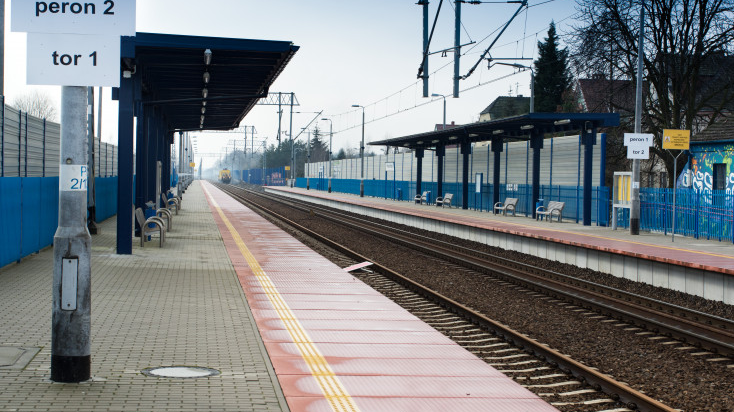Dwa perony przy dwutorowej linii kolejowej, w głębi widoczna lokomotywa spalinowa