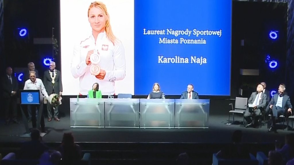 Widok na scenę z miejsc dla publiczności, na ekranie wyświetlony portret i nazwisko "Karolina Naja"