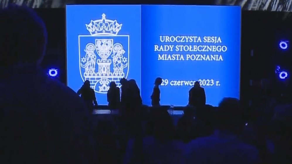 Sylwetki ludzi wstających z krzeseł na tle niebieskiego ekranu
