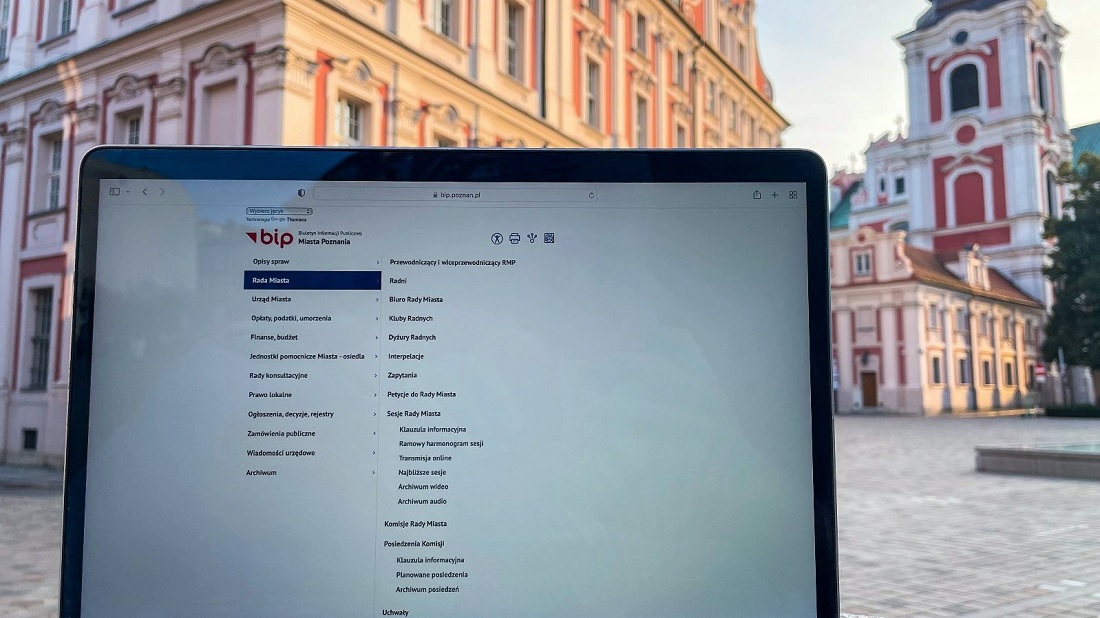 monitor laptopa z wyświetlona stroną, w tle plac i gmach w czerwono-białych kolorach - grafika artykułu