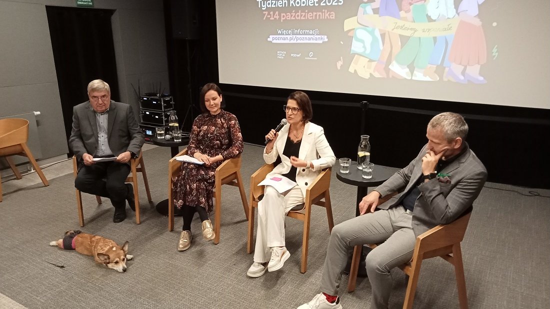 cztery osoby siedzą na krzesłach podczas konferencji prasowej, dwie kobiety w śrosku, z prawej i lewej mężczyźni, za nimi ekran z wyświetloną grafiką