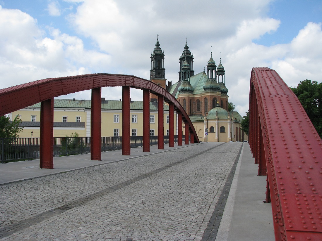 Most z brukowaną nwierzchnia, po obu stronach łukowate przęsła w koloze czerwonym, za mostem widoczna katedra poznańska - grafika artykułu