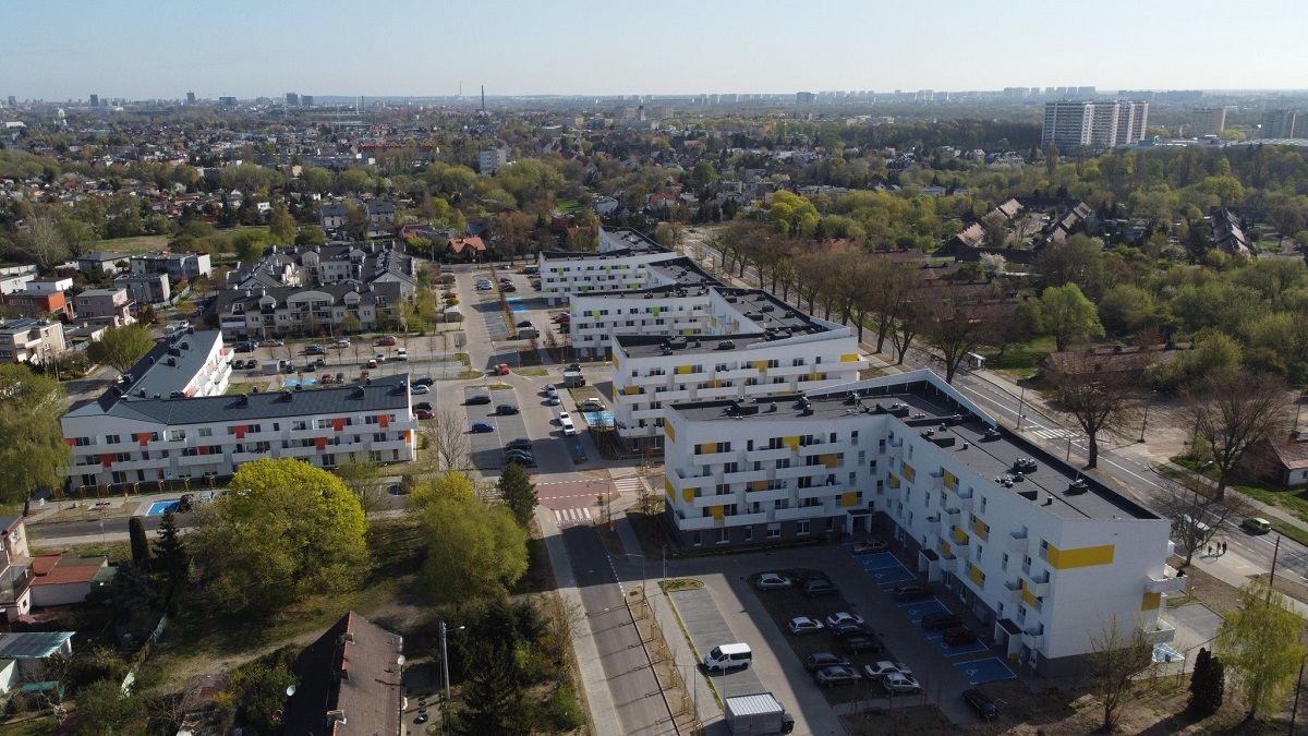 widok z lotu ptaka kilka bloków mieszkalnych czteropiętrowych za nimi drzewa teren zielony, dalej inne zabudowania - grafika artykułu