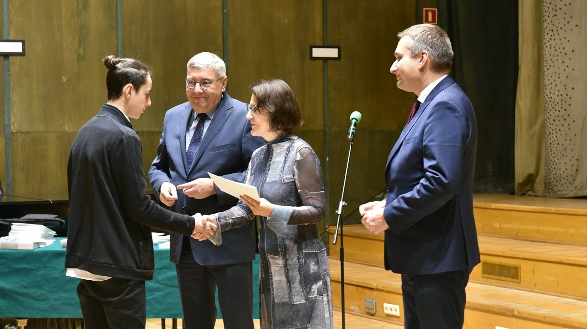 Uroczystość wręczenia nagród dla najlepszych uczenic i uczniów z Poznania, troje osób kobieta i dwóch mężczyzn składają gratulację jednemu z uczniów - grafika artykułu