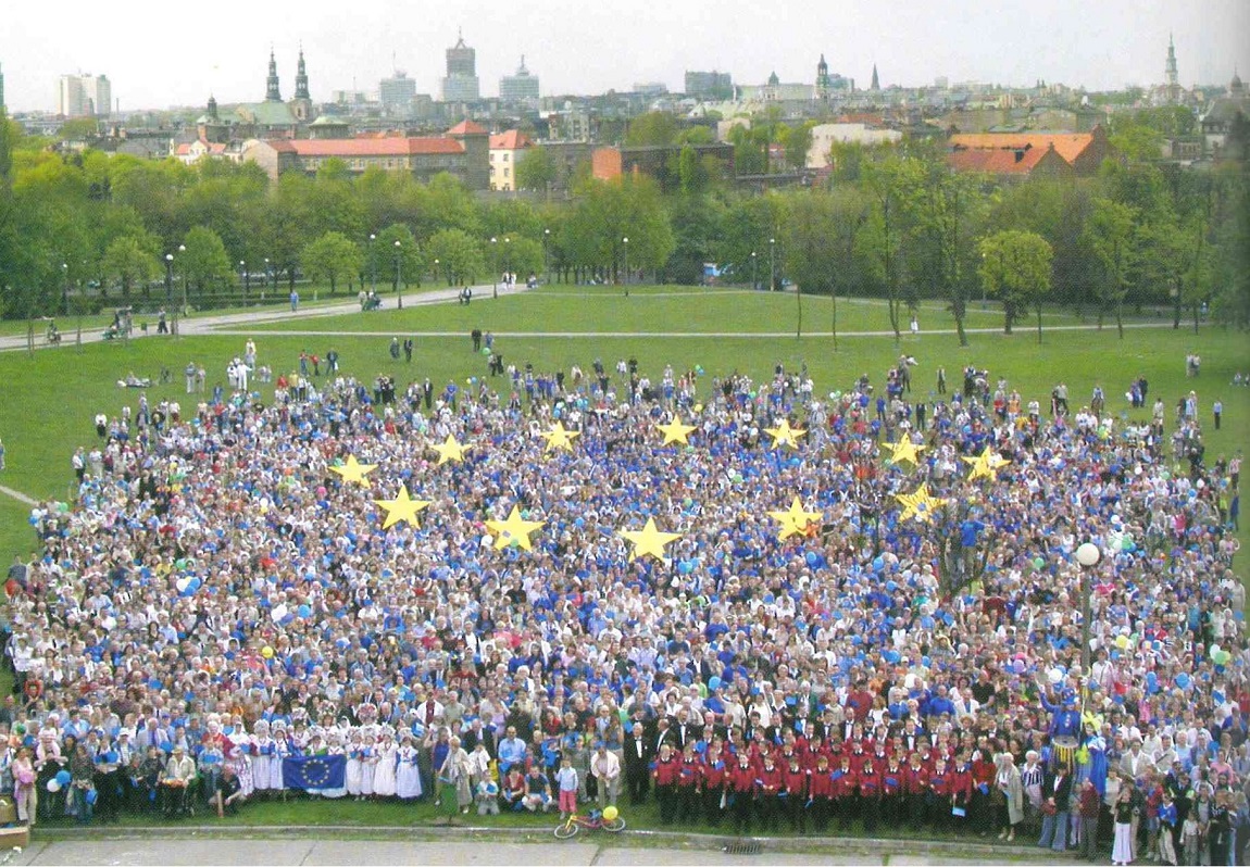 Duża grupa ludzi w parku, w tłumie żółte gwiazdy nawiązujące do flagi Unii Europekskiej - grafika artykułu