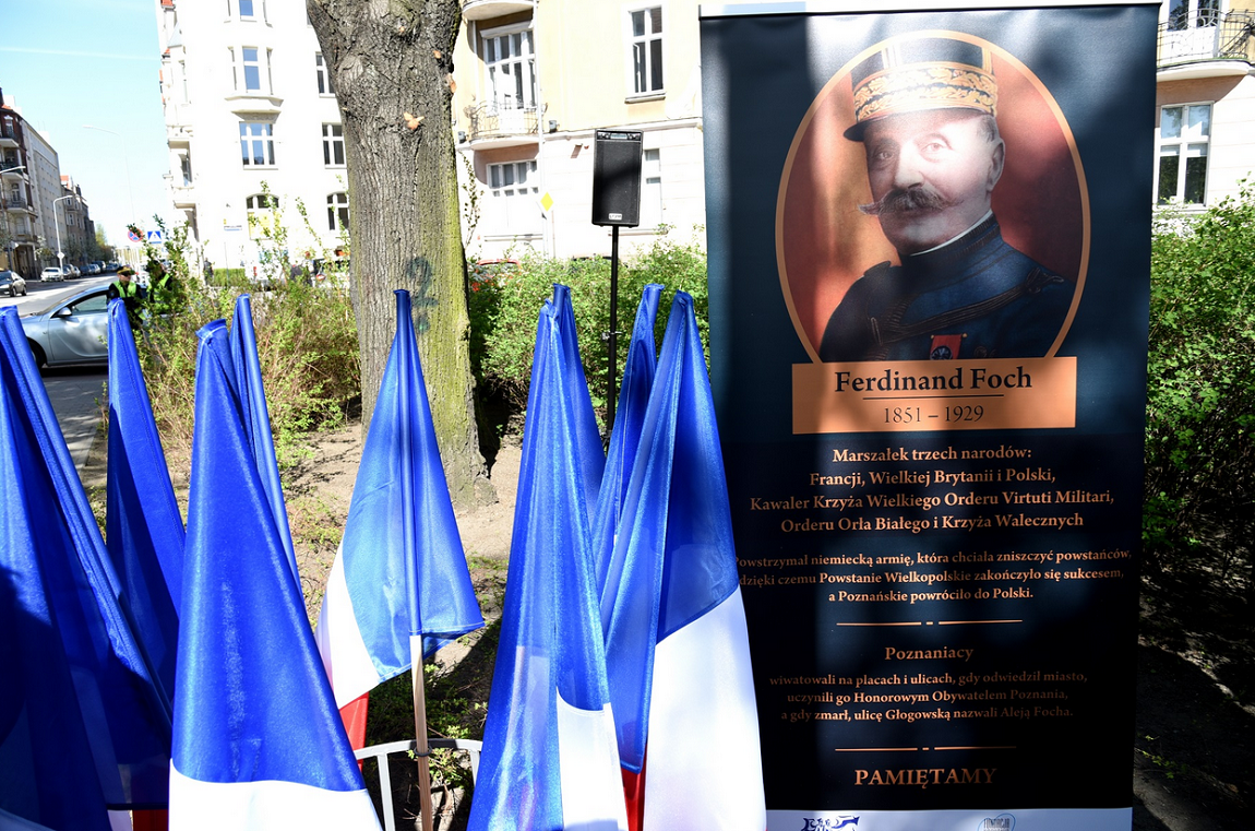 baner z wizrukiem marszałka Focha, ubrany w mundur, ma długie podkręcone wąsy, pod wizerunkiem informacja o nim, obok kilka flag Francji, za nimi drzewa i krzewy oraz kamienice - grafika artykułu