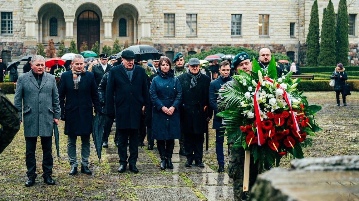 przedstawiciele władz rządowych i samorządowych stoją przed pomnikiem, przed nimi strażnik trzymający wiązankę - grafika artykułu