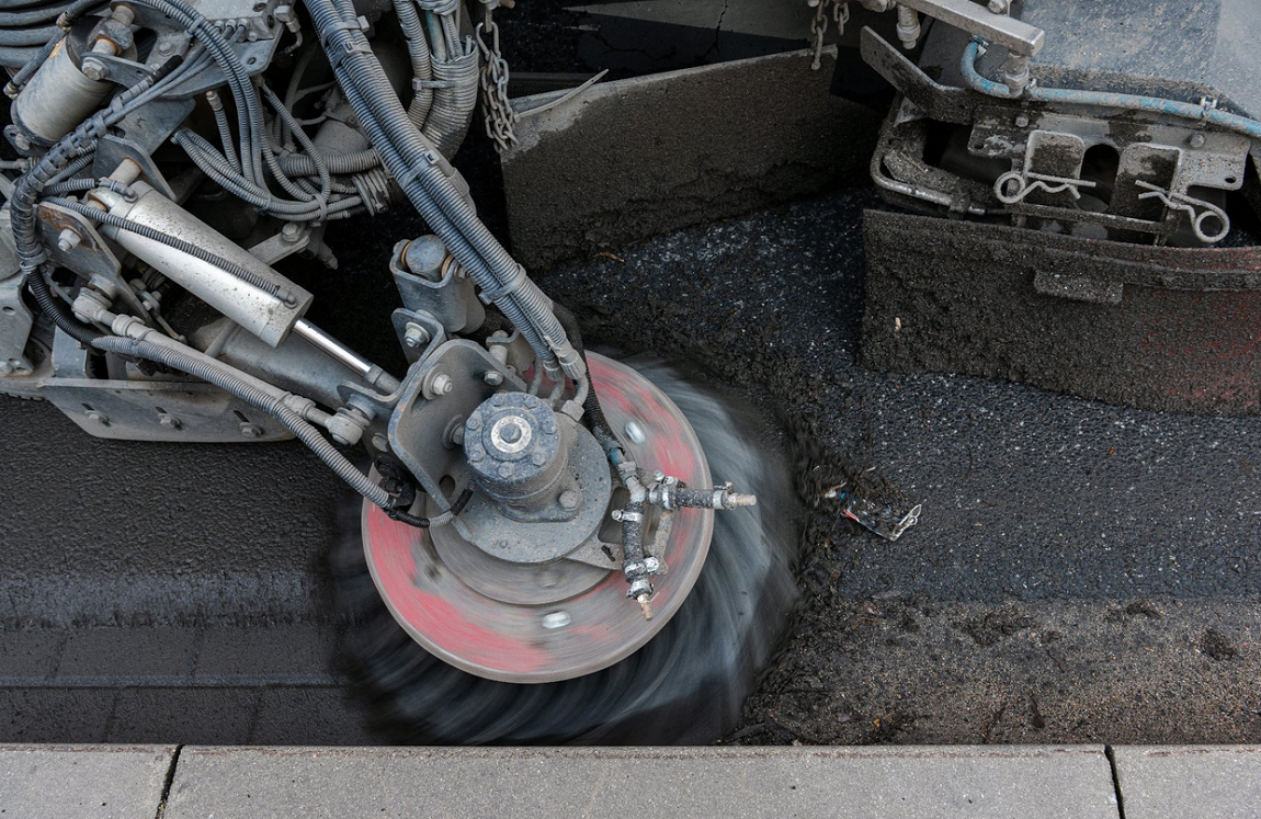 na dużym zbliżeniu maszyna sprzątająca ulice, mechaniczna szczotka zbiera nieczystości przy krawężniku - grafika artykułu