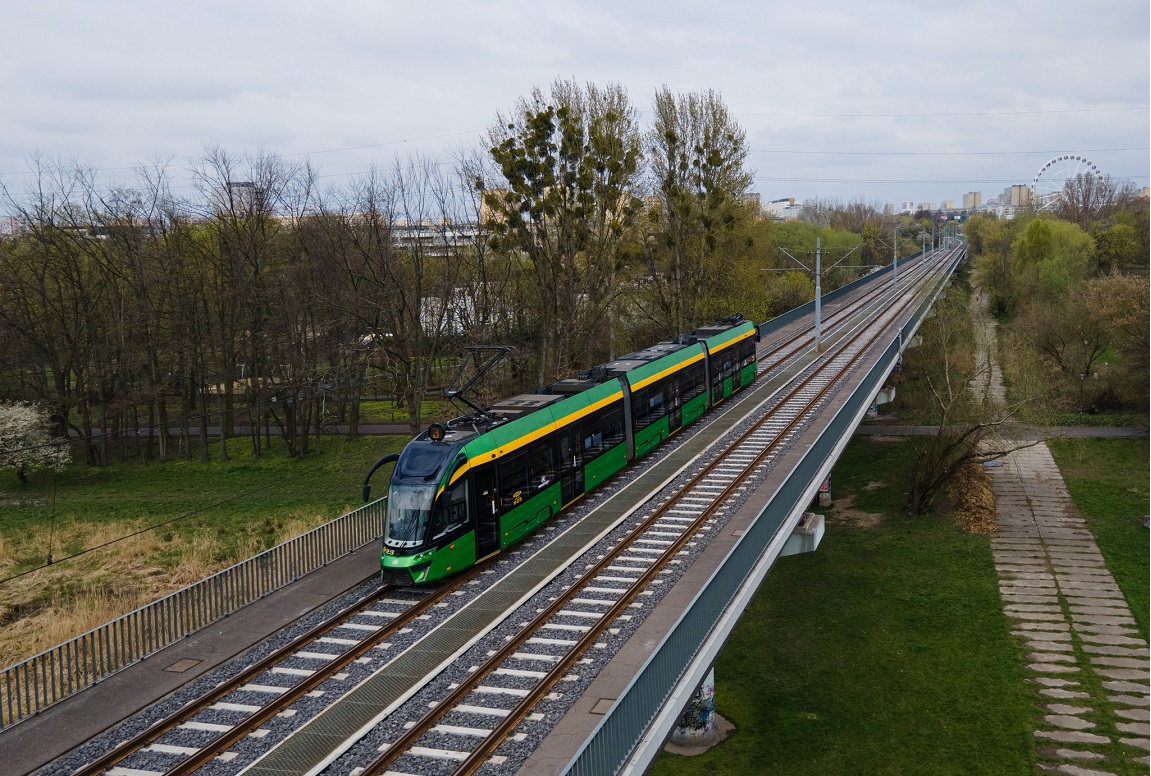 Tramwaj jadący po wiadukcie, pod wiaduktem trwa, obok wiaduktu drzewa - grafika artykułu