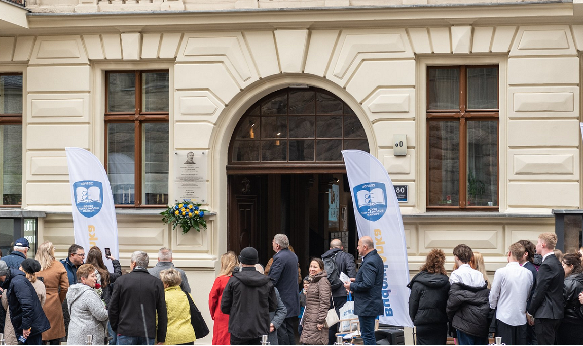 livzna grupa osób w różnym wieku kobiet i mężczyzn stoi przed zabytkową kamienicą w jasnym kolorze - grafika artykułu