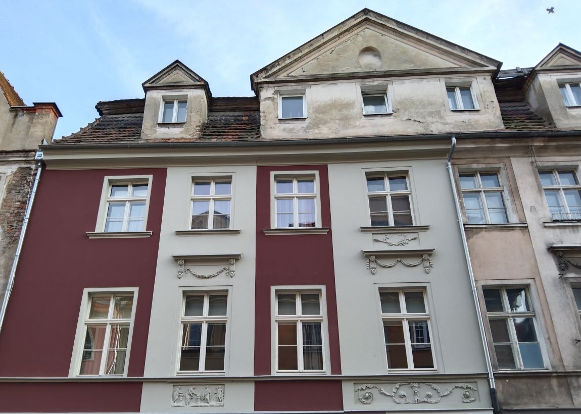 Fragment kamienicy, wyższe kondygnacje, elewacja częściowo pomalowana na różne kolory, część elewacji niepomalowana i nieodnowiona - grafika artykułu