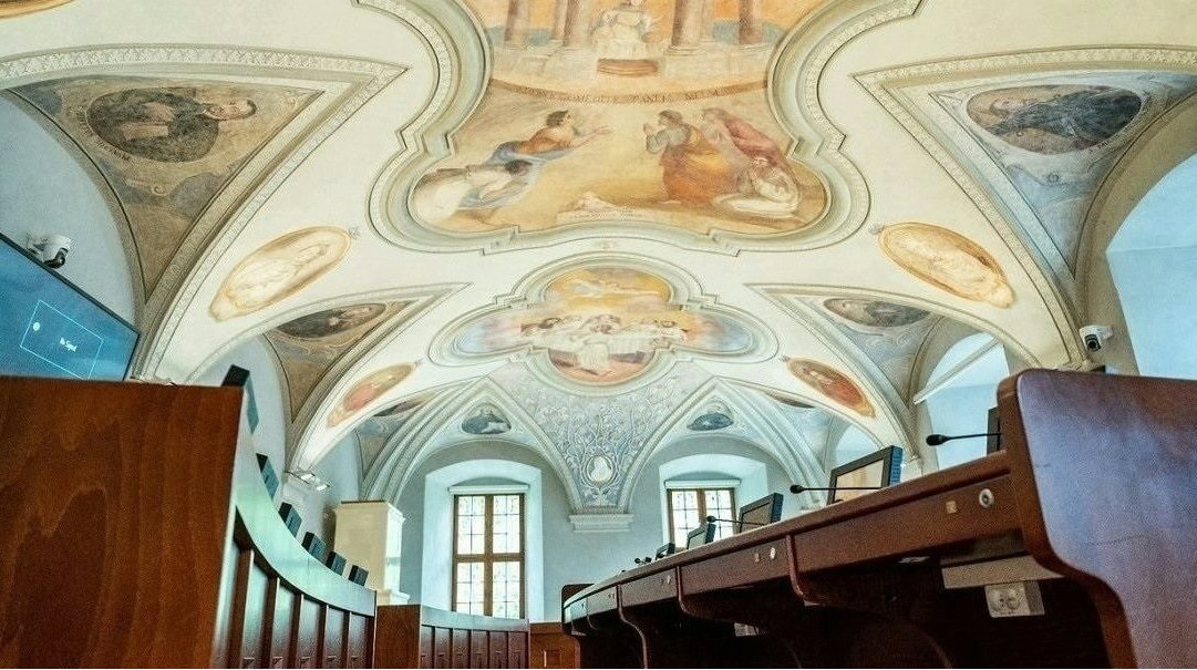 Sala sesyjna Rady Miasta Poznania, pusta, widoczne stanowiska radnych i zdobiące sufit zabytkowe freski - grafika artykułu - grafika artykułu