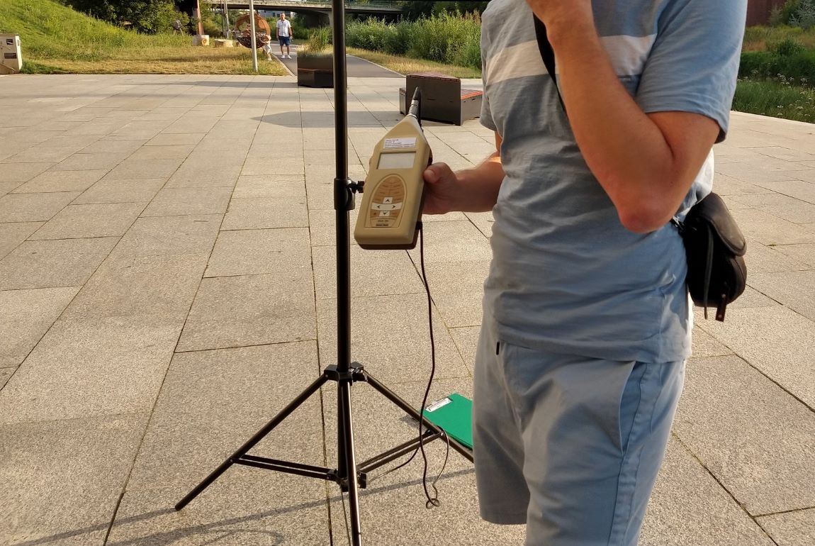 człowiek, nie widać twarzy, trzyma w ręku urządzenie do pomiaru hałasu - grafika artykułu