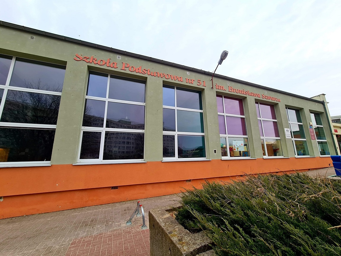 budynek szkolny, jednopoziomowy, z dużymi oknami, przed nim chodnik i niska roślinność - grafika artykułu