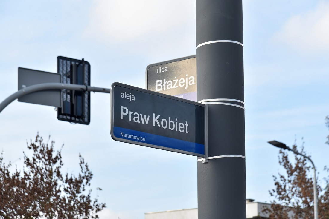 tablica z nazwą ulicy Aleja Praw Kobiet zawieszona na słubie, za nią tablica z nazwą ulicy Błażeja - grafika artykułu