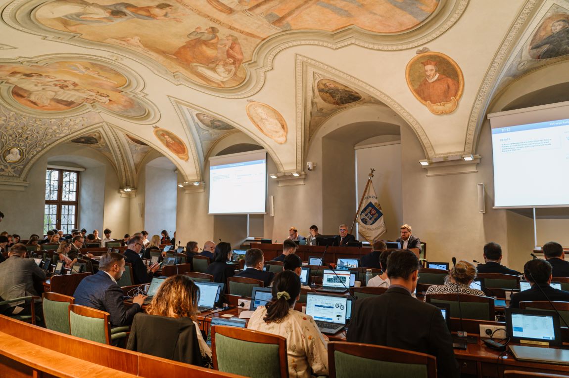 radni w sali sesyjnej na siedzą przy stanowiskach z monitorami i mikrofonami, przed nimi stół prezydialny przy którym siedzi kilku radnych z prezydium - grafika artykułu