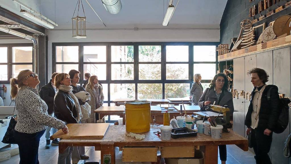 grupa osób zwiedza pomieszczenie warsztatu rzemieślniczego, na stołach pojemniki z klejem i deski