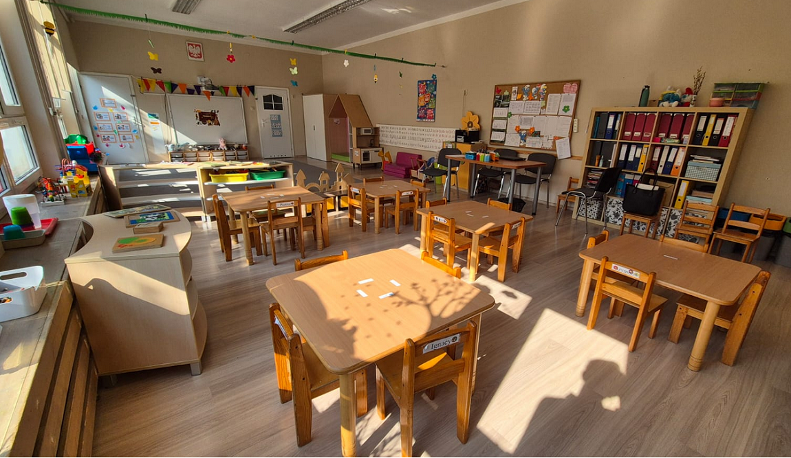 Jedna z sal przedszkola nr 130 w Poznaniu, widoczne stoliki z krzesłami, szafki, tablice, zabawki - grafika artykułu