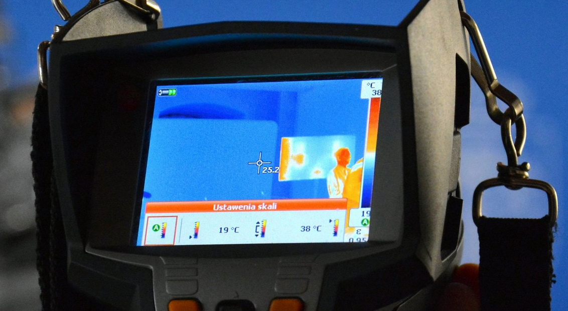kamera termowizyjna, a której ekranie wyświetla się obraz termowizyjny skanowanego pomieszczenia - grafika artykułu