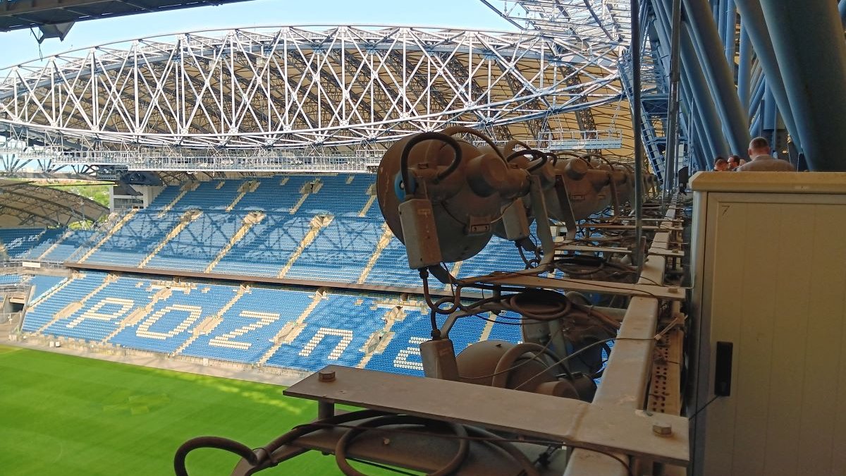 na pierwszym planie reflektory stadionowe, poniżej fragment zadaszenia, trybun i murawy