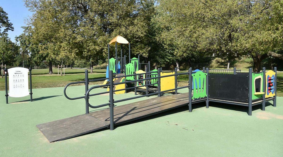 plac zabaw z urządzeniami dla dzieci z niepełnosprawnościami, obok tablica z alfabetem Braille'a - grafika artykułu