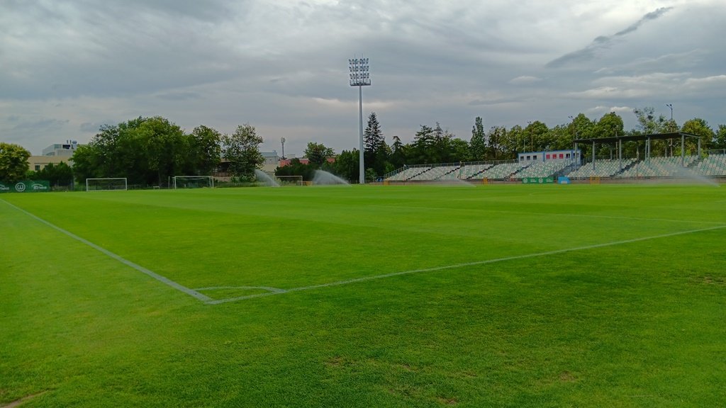 boisko trawiaste, widoczne oświetlenie i trybuny
