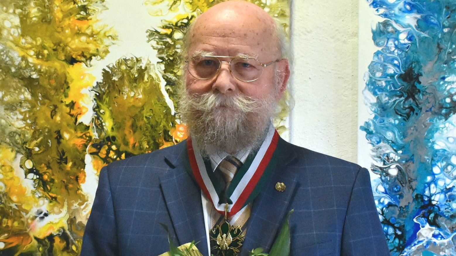 Antoni Rut - tytuł Zasłużony dla Miasta Poznania 2025 - starszy mężczyna, z łysiną, siwą brodą i wąsami, ma okulary, nosi marynarkę, na szyi ma zawieszony order z orłem