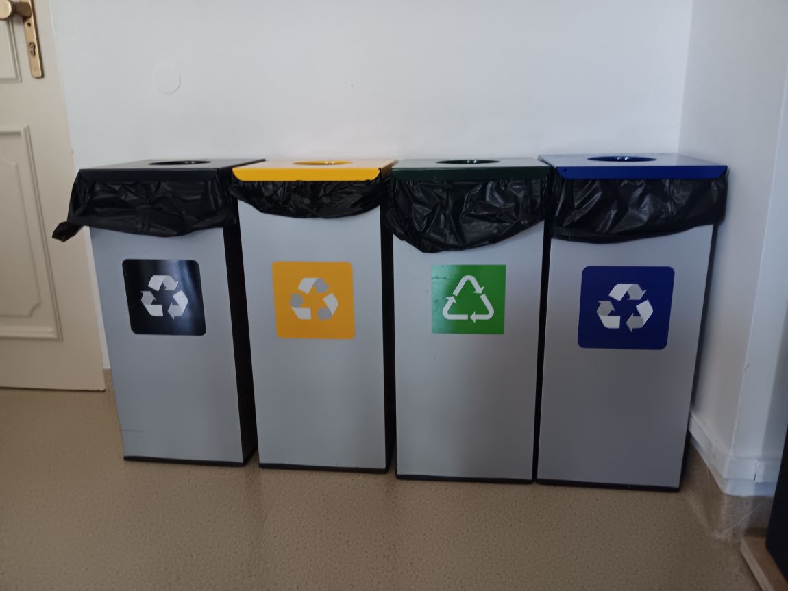 cztery pojemniki do segregacji różnego rodzaju odpadów, stoją w rzędzie przy ścianie - grafika artykułu