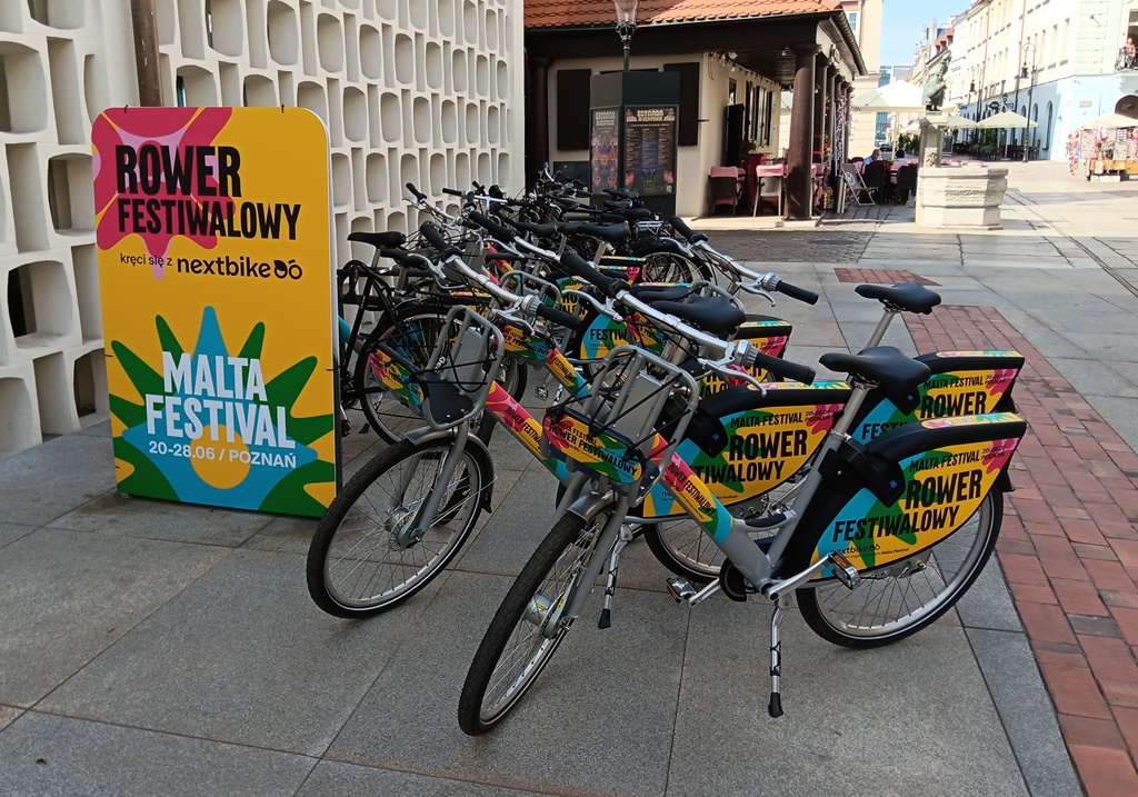 około kilkunastu rowerów miejskich ustawionych blisko siebie, obok baner z logo festiwalu malta, nextbike i napisem rower festiwalowy, rowery stoja na płycie Starego Rynku - grafika artykułu