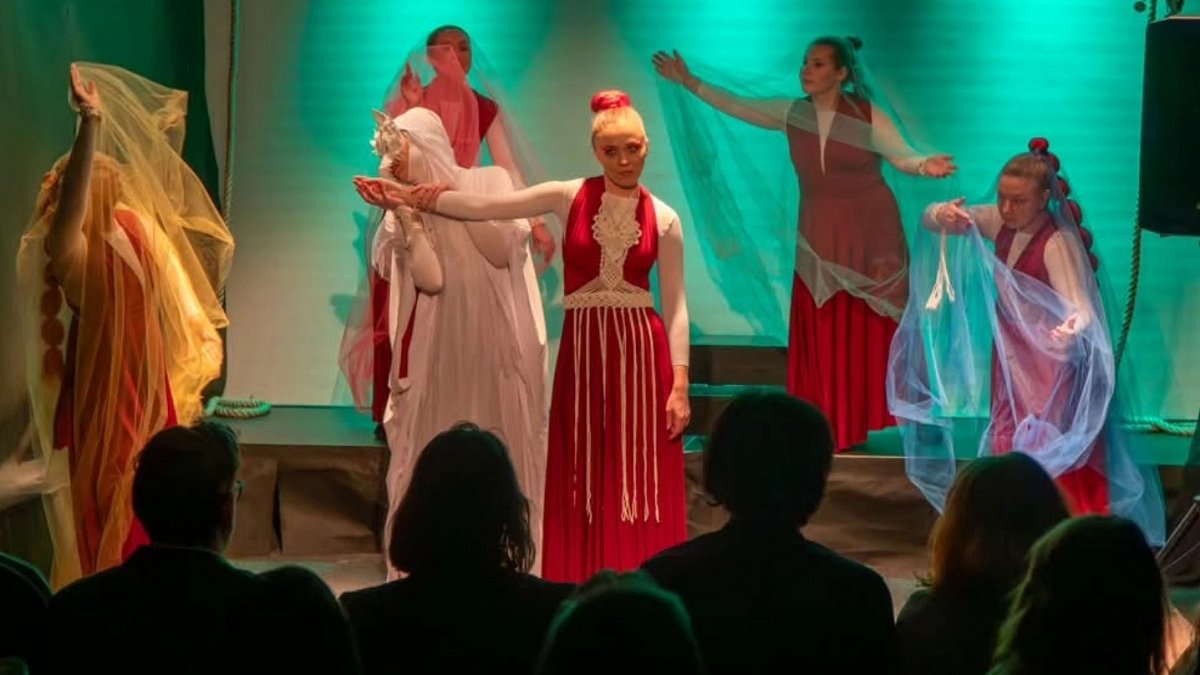 spektakl teatralny, na scenie kobiety ubrane w czerwono białe stronie, niektóre z nich mają zarzucone welony