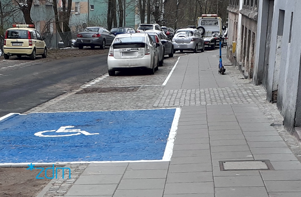 ulica, przy chodnikach zaparkowane samochodwy, widoczna wolna koperta dla samochodów osób niepełnosprawnych - grafika artykułu