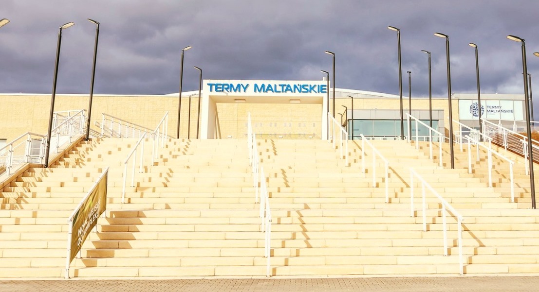 wejście do budynku Term Maltańskich, wysokie, szerokie schody, na ich szczycie wejście z dużym napisem nad nim TERMY MALTAŃSKIE, na schoda stoją latarnie - grafika artykułu