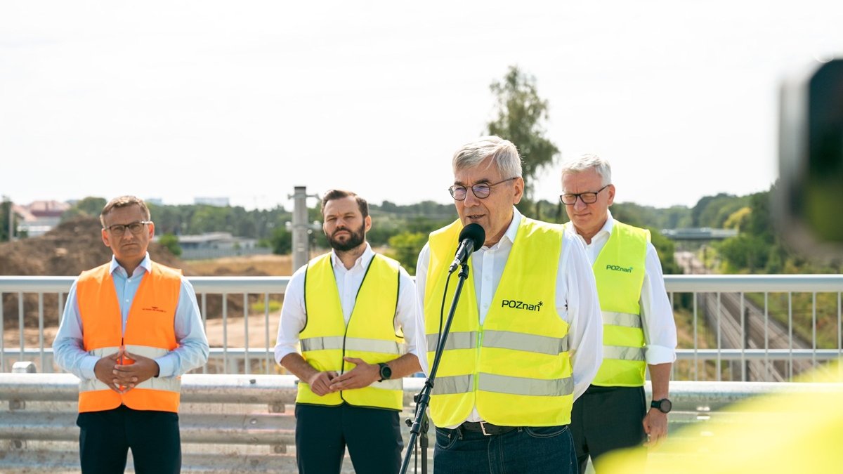 czterej mężczyźni stoją na wiadukcie, mają odblaskowe kamizelki, jedna z tych osób stoi przy mikrofonie ze stojakiem