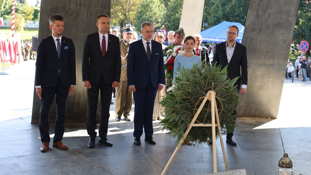 przy pomniku kilka osób stoi podczas uroczystości składania kwiatów