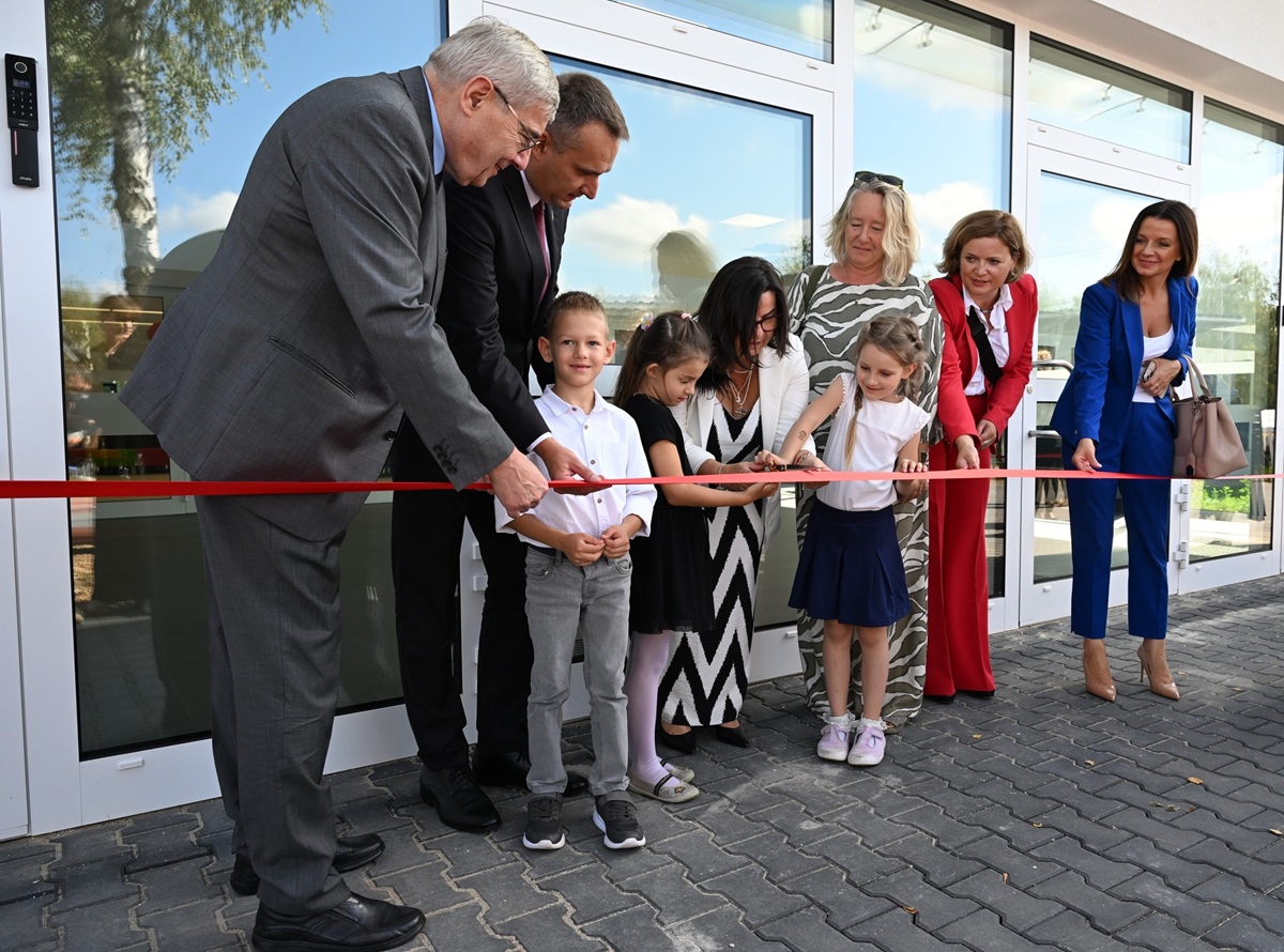 grupa osób dorosłych i dzieci przecina wstęgę przed wejściem do szkoły - grafika artykułu