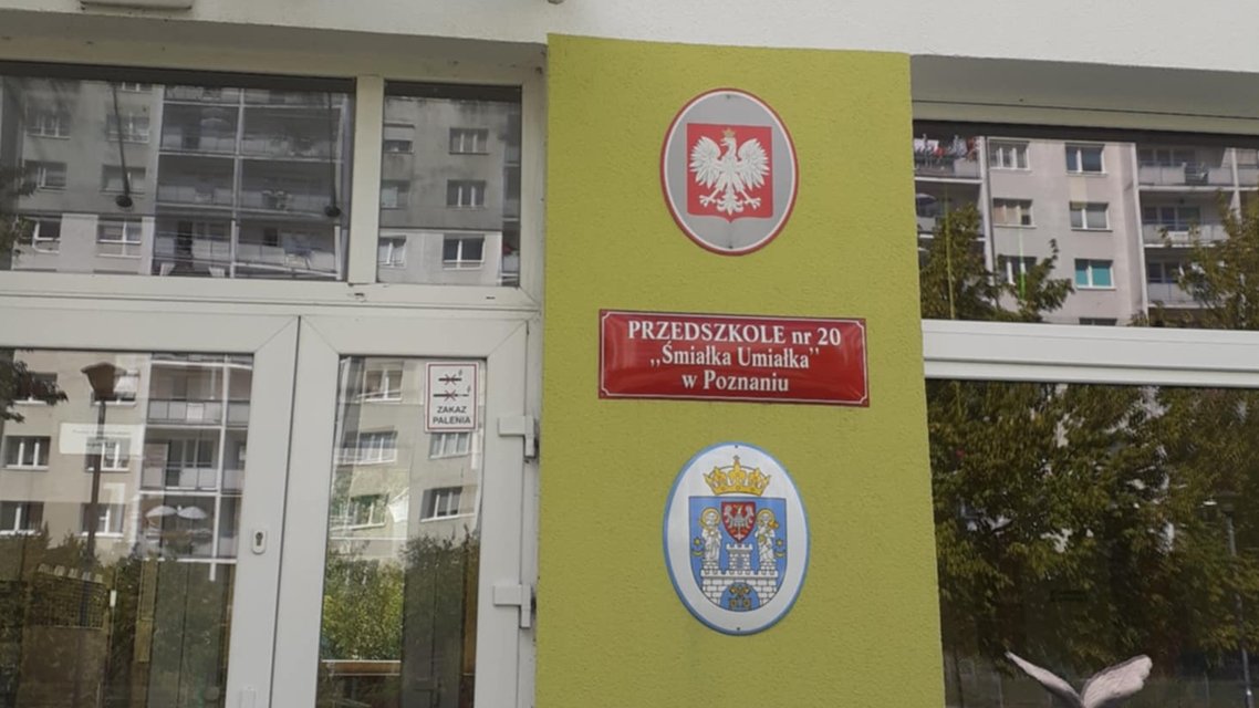 przed wejściem do przedszkola na ścianie godło Polski, tablica z nazwą przedszkola i herb Poznania