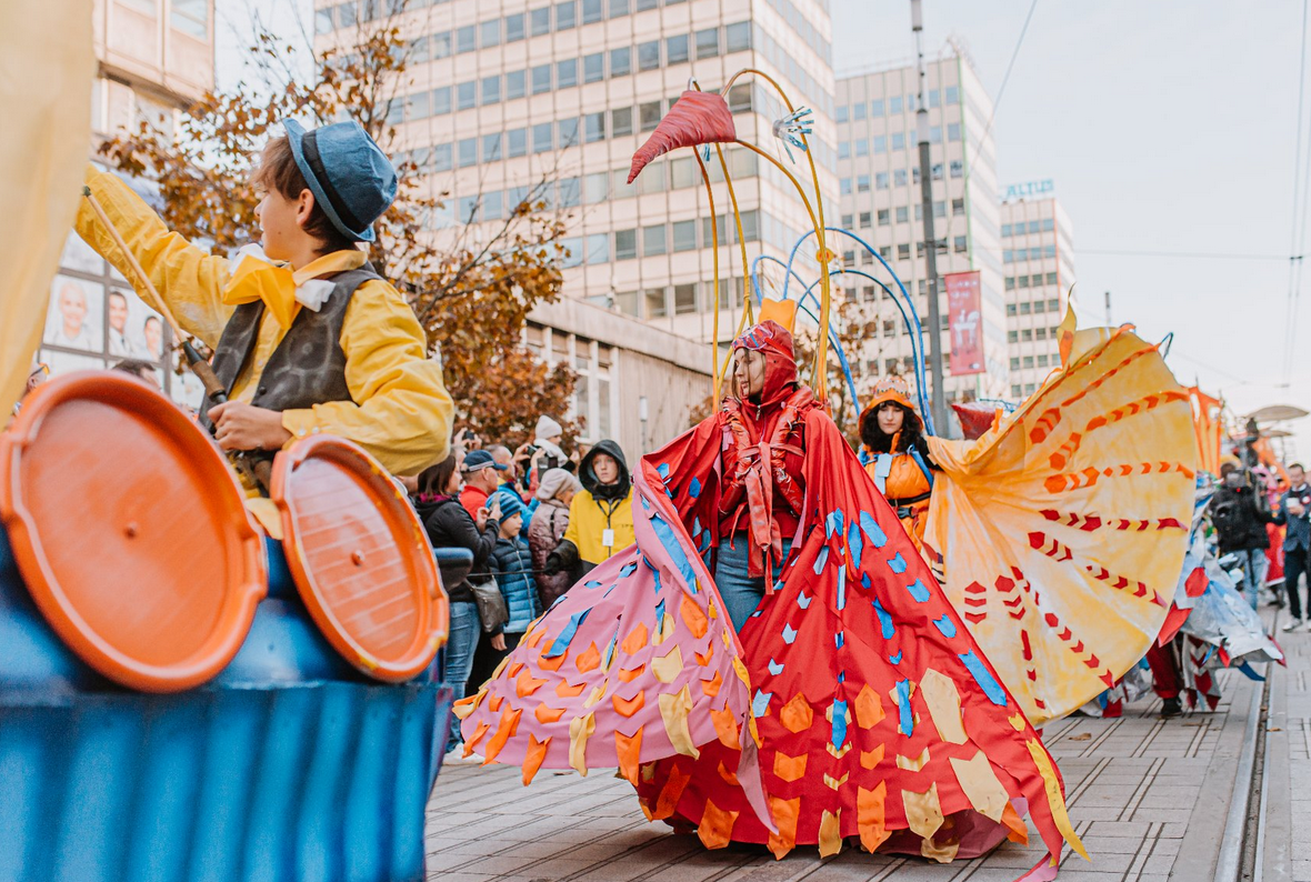 korowód idący przez ulicę w korowodzie osoby w barwnych strojach wzdłuż ulicy ustawieni ludzie oglądający korowód - grafika artykułu