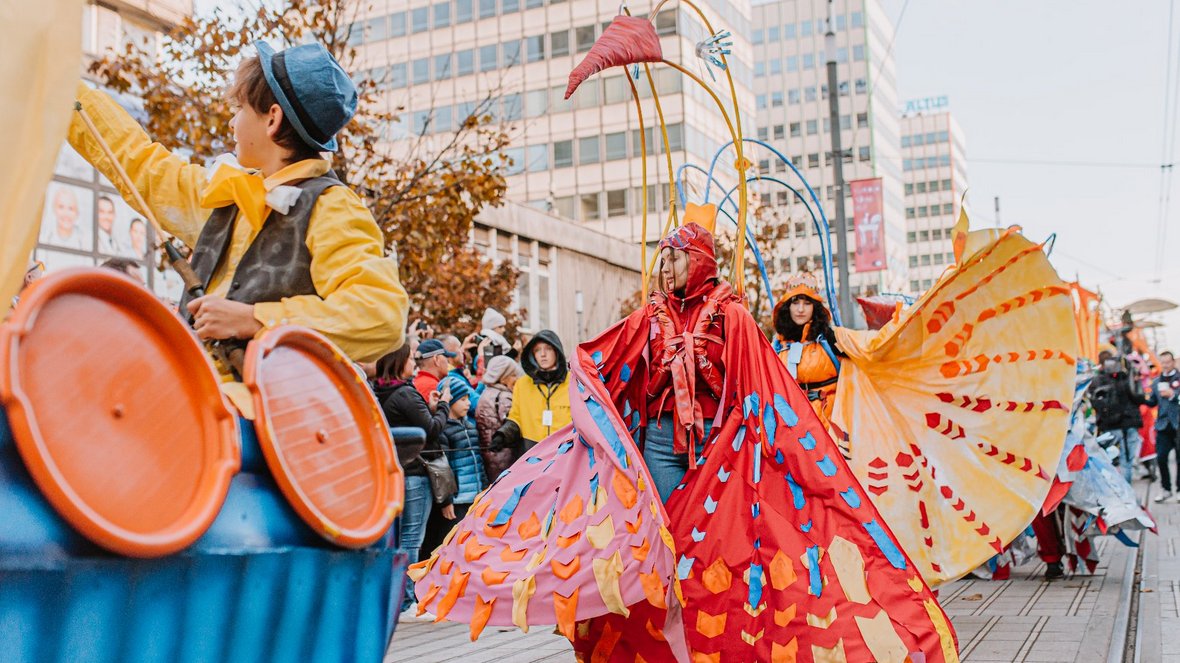 korowód idący przez ulicę w korowodzie osoby w barwnych strojach wzdłuż ulicy ustawieni ludzie oglądający korowód