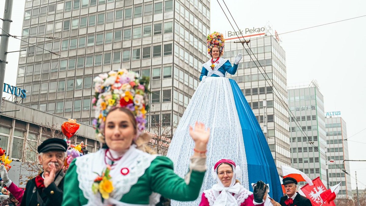 fragment korowodu idącego przez ulicę wodoczne kobiety i mężczyźni w strojach bamberskich jedna z uczestniczek w stroju bamberskim na podwyższeniu